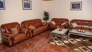 A living room with brown leather sofas, a coffee table, and a patterned rug. - Rest Guest House (Harare)