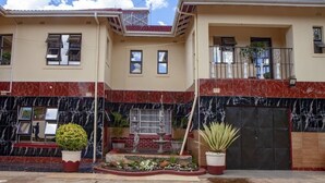 A two-story building with a balcony, a fountain, and potted plants. - Rest Guest House (Harare)