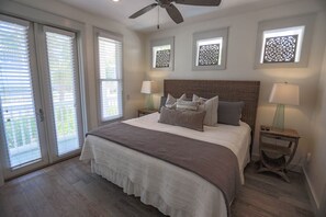 A bedroom with a large bed, two bedside tables with lamps, a ceiling fan, and decorative wall panels.