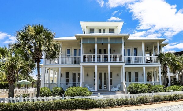 A two-story house with a balcony, white picket fence, and palm trees.