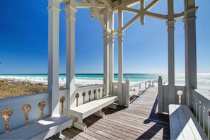 Un muelle de madera con barandas y bancos blancos que da a una playa.