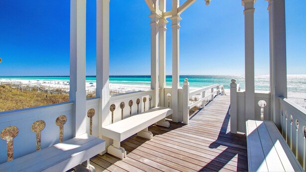 A wooden deck with white railings and benches overlooking a beach.