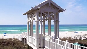 A beach gazebo with a white structure, a wooden deck, and a view of the ocean.