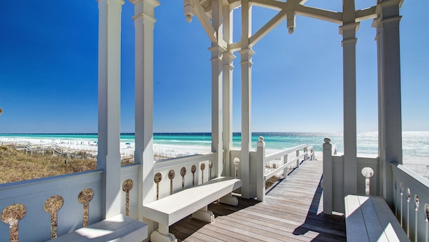 A wooden deck with white railings and benches overlooking a beach.