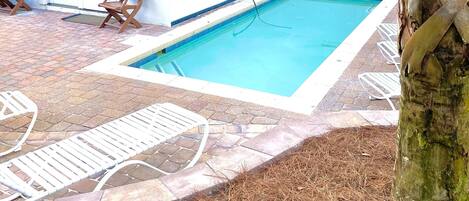 A pool area with a tiled deck, lounge chairs, and a palm tree.