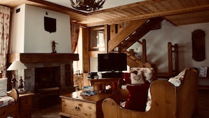 Un intérieur chaleureux avec des boiseries, une cheminée, un téléviseur et un escalier.