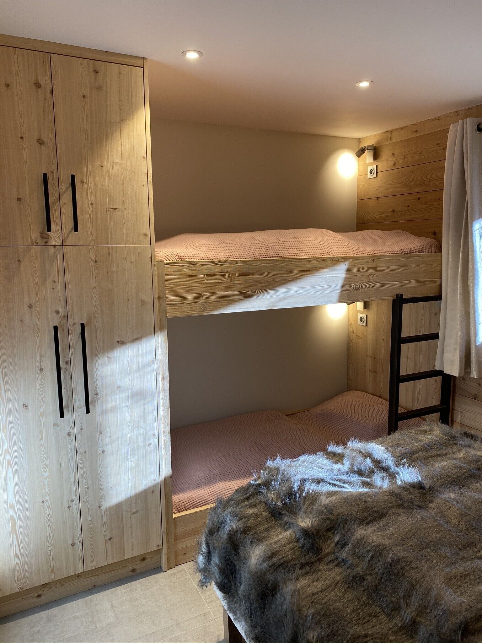 Een slaapkamer met stapelbed, houten wanden, een kledingkast en een bont kleed.