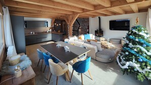 Un amplio salón con techo de madera, una mesa de comedor con sillas, un sofá, un árbol de Navidad y una cocina al fondo.