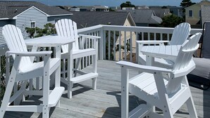 A deck with white Adirondack chairs and a table, overlooking a residential area with houses and a clear blue sky. - Beach Goals! 4 bedroom 2.5 bath home, just a 5 minute walk to beach!!! (Sunset Beach)