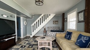 A living room with a staircase, a television, a patterned rug, and a sofa with decorative pillows. - Beach Goals! 4 bedroom 2.5 bath home, just a 5 minute walk to beach!!! (Sunset Beach)