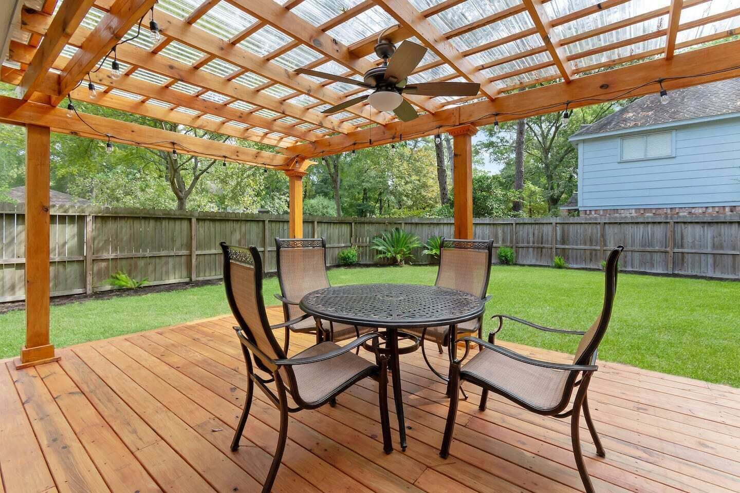 A covered patio with a round table and four chairs, a ceiling fan, and a wooden deck.