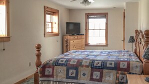 Una camera da letto con un letto in legno, una cassettiera, una televisione e due finestre.