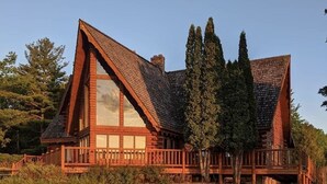 Une cabane en rondins dotée d’une grande fenêtre centrale, d’une terrasse et d’un toit en pente.