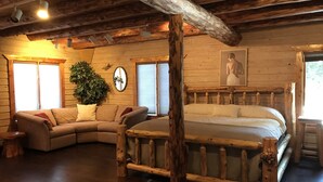 L’intérieur d’une cabane en rondins, avec un grand lit, un canapé et un plafond en bois.