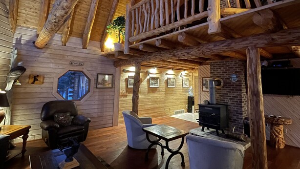 L’intérieur d’un chalet rustique, avec des poutres en bois, une cheminée, un coin repas et une sculpture d’aigle fixée au mur.
