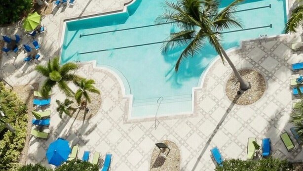 Ovenudblik over et resortområde med en stor swimmingpool, omgivet af liggestole og palmer.