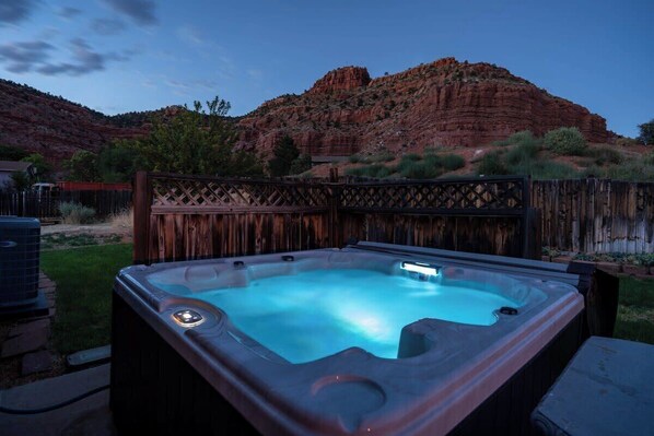 A hot tub in a backyard with a wooden fence and a mountainous backdrop.