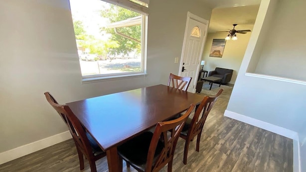 A dining area with a wooden table and chairs, a window with blinds, a door with a decorative glass panel, and a ceiling fan. - Family Home in Kanab w/ private Hot Tub, Near Zion (Kanab)