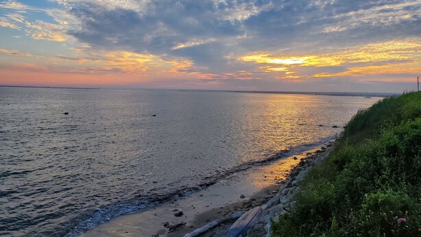 A beach with a calm sea, a rocky shoreline, and a grassy area with vegetation.