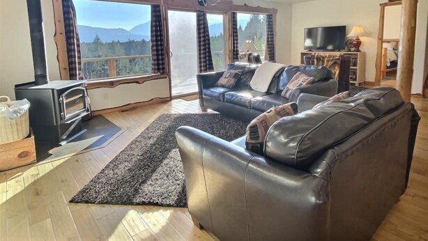 A cozy living room with a fireplace, a leather sofa, and large windows offering a mountain view. - Elk Ridge (Packwood)