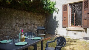 An outdoor dining area with a table set for two, surrounded by stone walls and greenery.