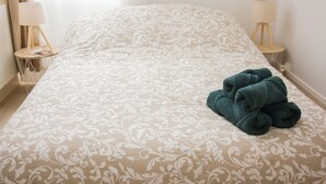 A neatly made bed with a patterned bedspread, two bedside lamps, and a stack of folded towels on the right side.