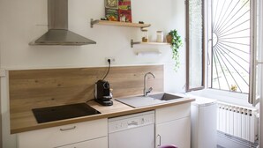 A modern kitchen with a stainless steel range hood, wooden countertop, built-in dishwasher, and a window with a metal grill.