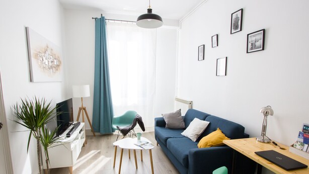 A modern living room with a blue sofa, a wooden desk, a white coffee table, and a green chair.