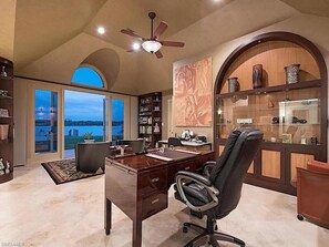 Work in comfort with a large desk and ergonomic chair, surrounded by a high ceiling and natural views.