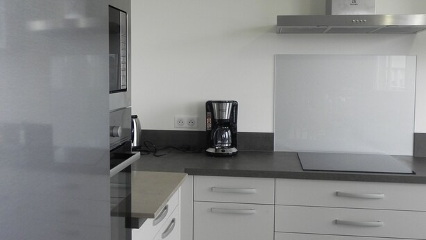 A modern kitchen with white cabinets, a stainless steel refrigerator, a coffee maker, and a microwave.