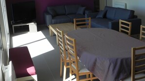 A modern living room with a sofa, a TV, a dining table with chairs, and a bench.