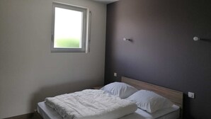 A bedroom with a single bed, a window, and a dark wall.