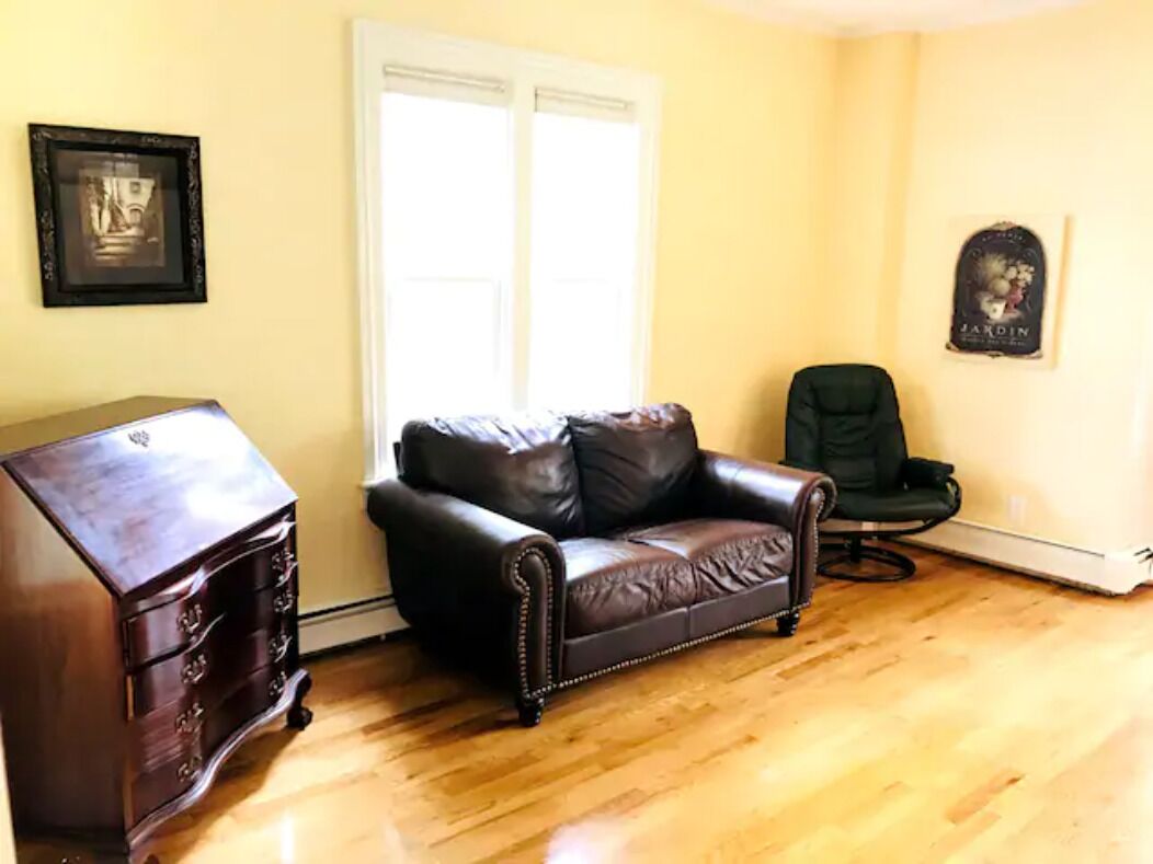 A room with a brown leather sofa, a wooden dresser, and a black chair.