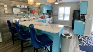 A modern kitchen with a central island, blue chairs, and pendant lighting.
