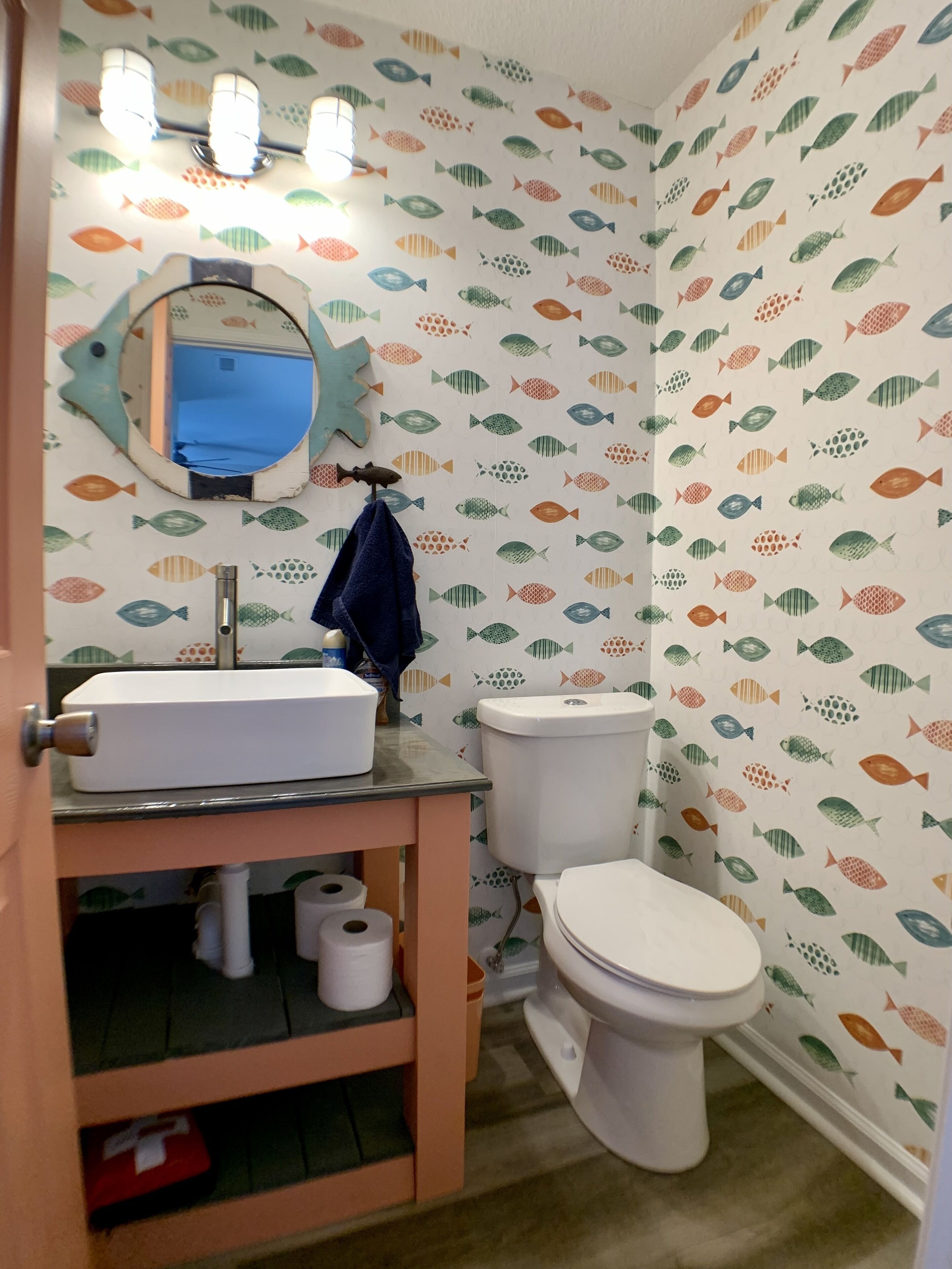 A bathroom with a white sink, a mirror, and a toilet. The walls are decorated with a fish pattern.