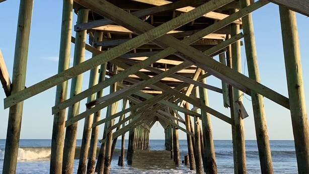 A wooden pier extending into the ocean with a clear view of the water and waves.