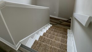 A stairwell with a textured carpet, a chandelier, and a window with a view of the outside.