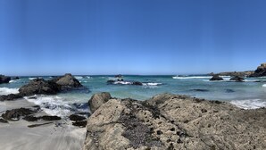 Eine felsige Küstenlinie mit brechenden Wellen, blauem Himmel und einem Sandstrand.