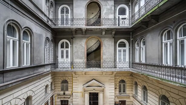 A multi-story building with a central courtyard, featuring arched windows and balconies with wrought iron railings.