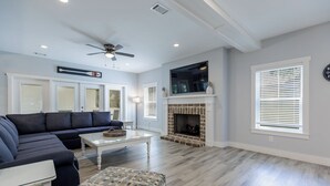 A living room with a sectional sofa, a patterned ottoman, a fireplace, and a ceiling fan. - Walk to beach-8BR w/ private pool-Sleeps 24-Ideal for groups and multi-families (Hilton Head Island)