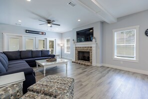 Ein Wohnzimmer mit Ecksofa, einem gemusterten Hocker, einem Kamin und einem Deckenventilator.