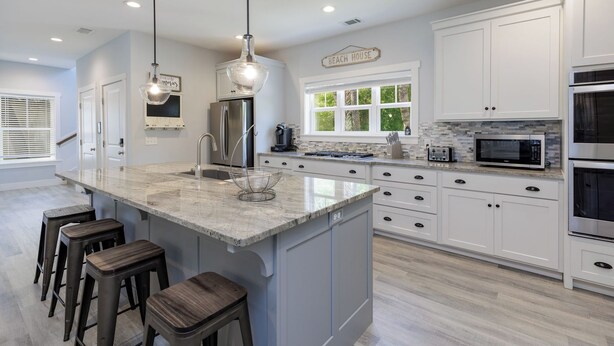 A modern kitchen with white cabinetry, a large island with stools, stainless steel appliances, and a 'Beach House' sign. - Walk to beach-8BR w/ private pool-Sleeps 24-Ideal for groups and multi-families (Hilton Head Island)