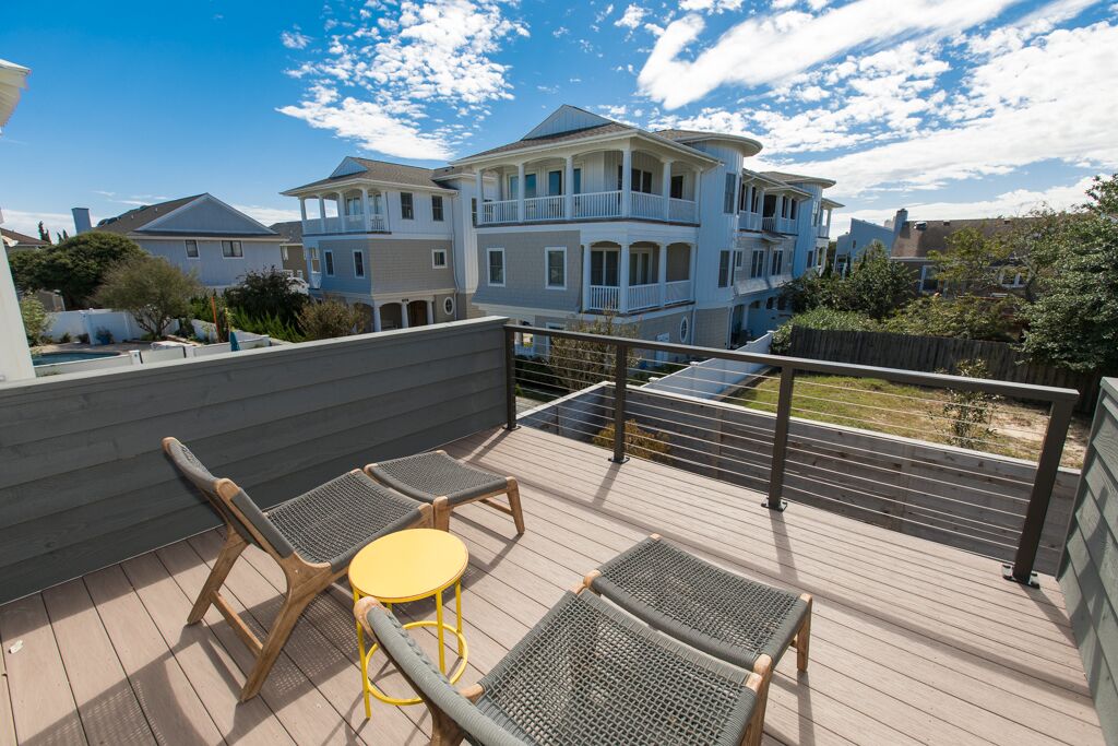 Um terraço no telhado com cadeiras de vime e uma mesa pequena, com vista para uma casa grande com várias varandas.