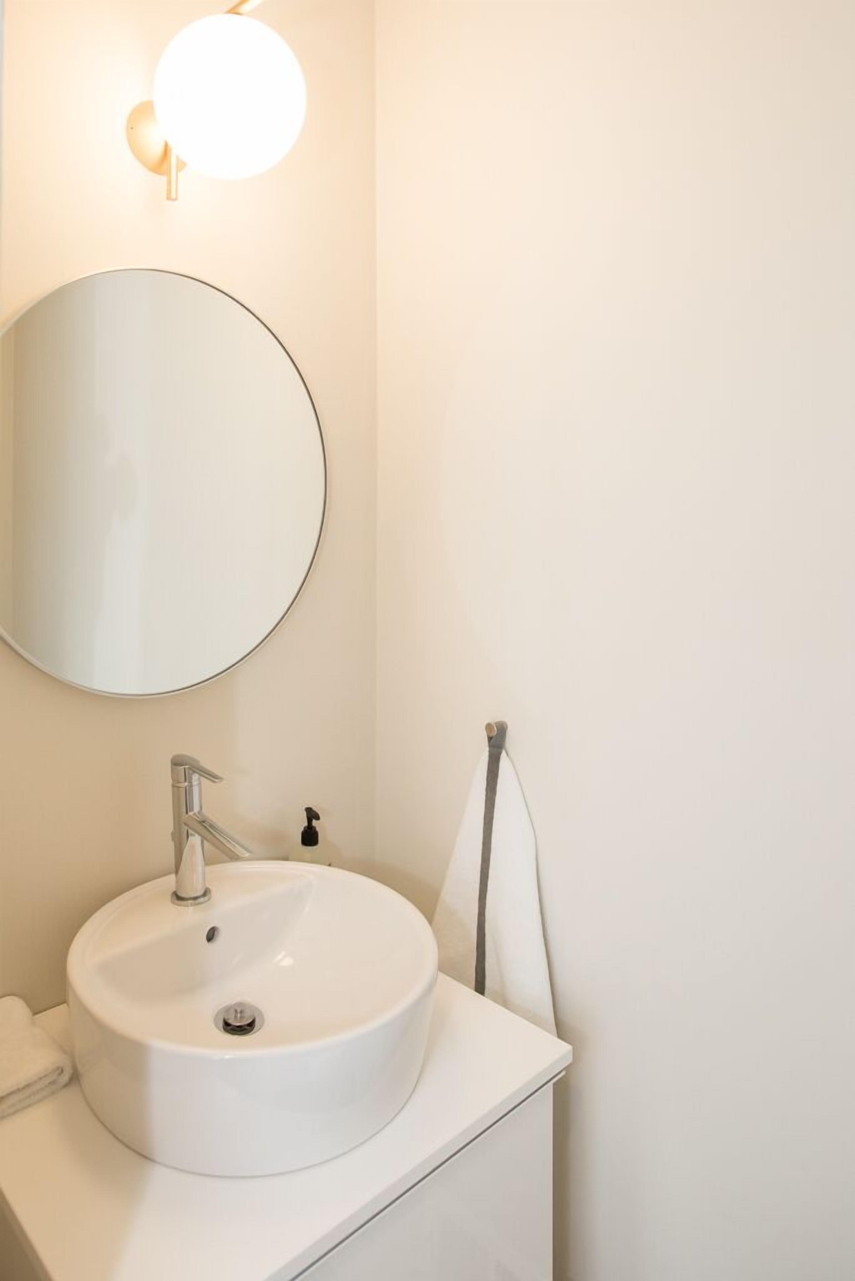 Een badkamer met een ronde spiegel, een witte wastafel en een handdoekrek.