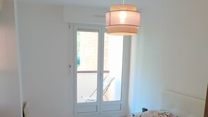 A room with a bed, a window, and a hanging light fixture. - Cabourg: Quiet apartment overlooking a park (Cabourg)