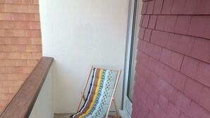 A corner of a room with a wooden bench, a window with a red brick exterior, and a white wall. - Cabourg: Quiet apartment overlooking a park (Cabourg)