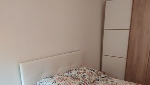 A bedroom with a bed, a wooden wardrobe, and a hanging light fixture. - Cabourg: Quiet apartment overlooking a park (Cabourg)