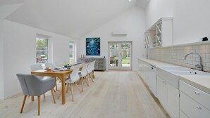 Una cocina moderna con armarios blancos, un comedor con mesa y sillas de madera, y un amplio ventanal con vistas a un jardín.