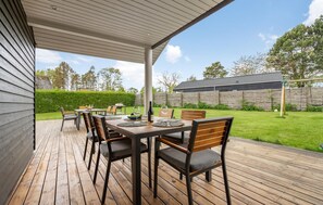 Une terrasse extérieure dotée d’une plateforme en bois, d’un espace salon couvert et offrant une vue sur un jardin avec une haie et une clôture en bois.