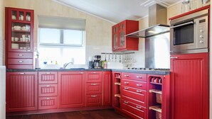 A kitchen with red cabinets, a stainless steel oven, and a window above the sink.